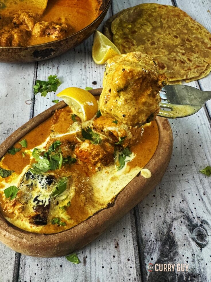 Salmon tikka masala in a serving bowl with a piece of salmon tikka on a fork.