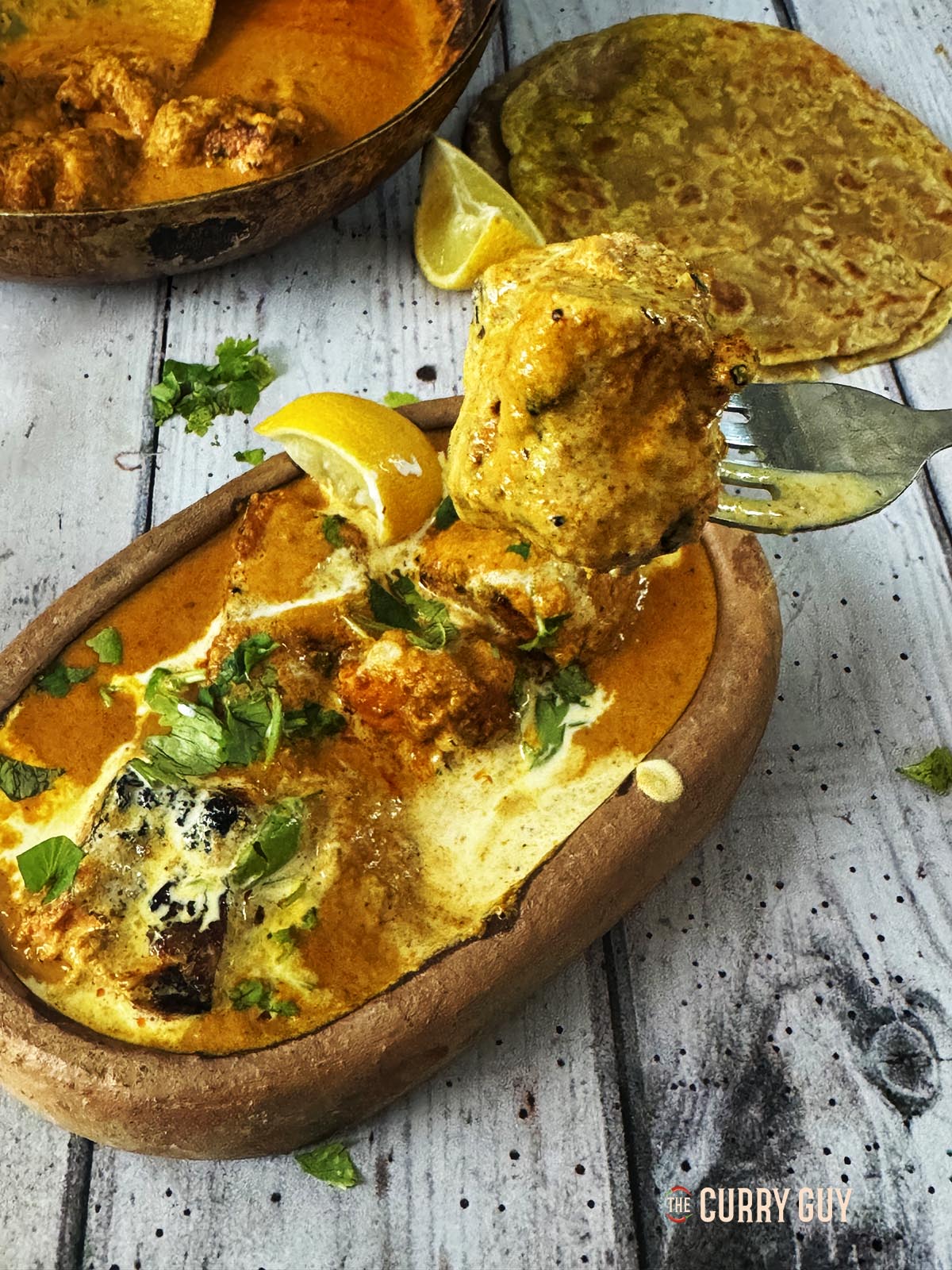 Salmon tikka masala in a serving bowl with a piece of salmon tikka on a fork.