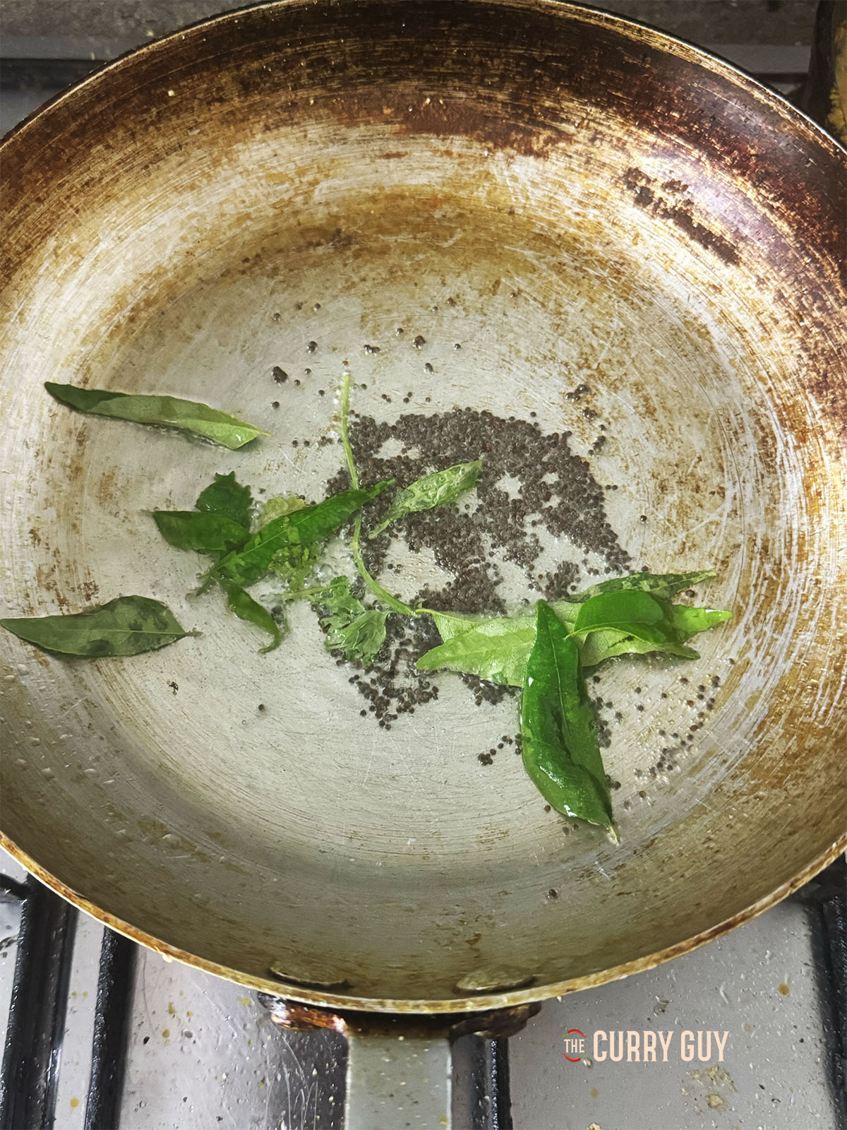 Infusing the mustard seeds and curry leaves into hot oil in a pan.