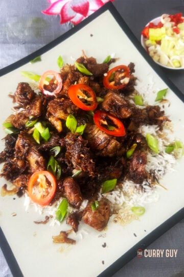 Sticky pork belly on a bed of rice and garnished with red chillies and spring onions.