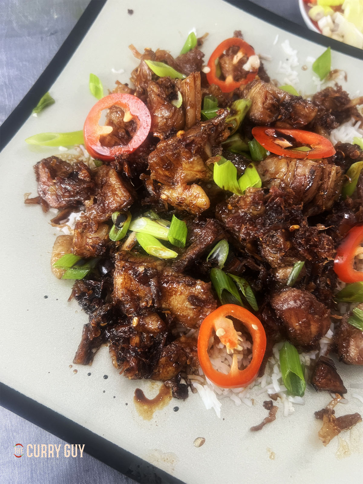 ~Sticky pork belly over a bed of white rice and garnished with sliced red chillies and spring onions.