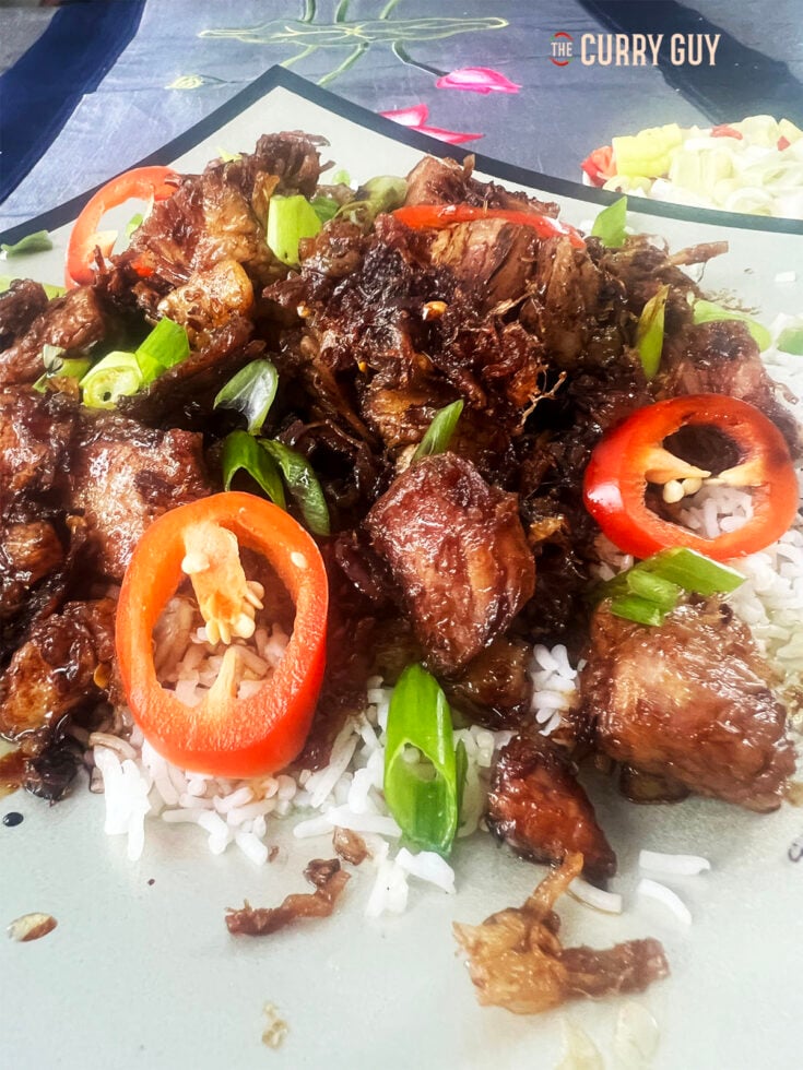 Sticky pork belly on a bed of white rice, garnished with red chillies and spring onion.