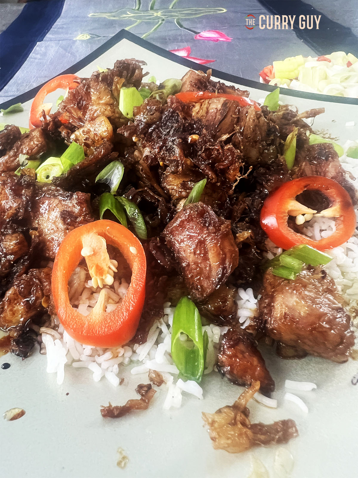 Crispy pork belly on a serving plate with rice and garnished with sliced red chillies and spring onions.