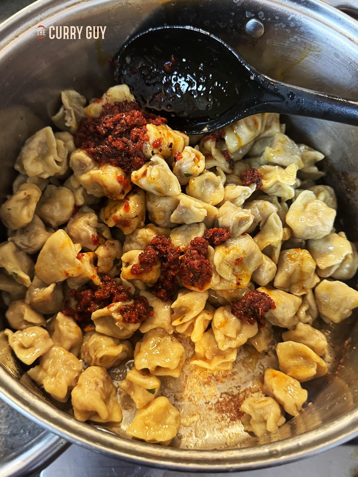 Adding the cooked pasta dumplings to the browned butter and then stirring in some of the red pepper sauce.