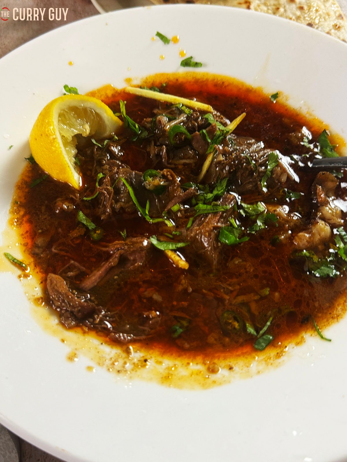 Beef nalli nihari in a serving bowl topped with ginger, coriander (cilantro) chillies and lemon juice.