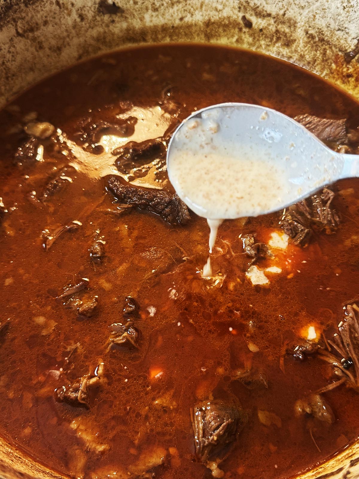 Adding the slurry to thicken the sauce.