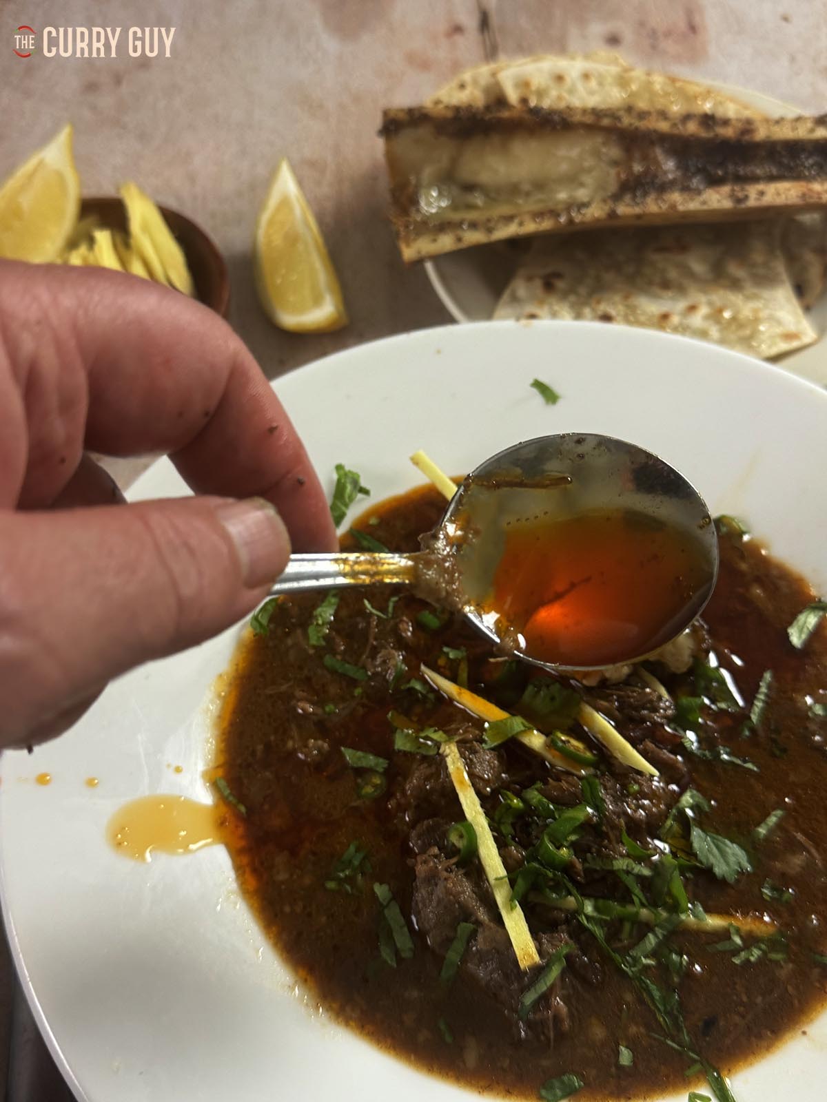 Adding the red, seasoned oil to a bowl of nalli nihari at the table.