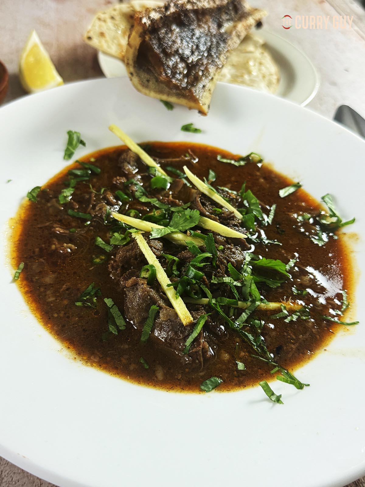 Beef nalli nihari in a serving bowl, garnished with julienned ginger, green chillies and chopped coriander.