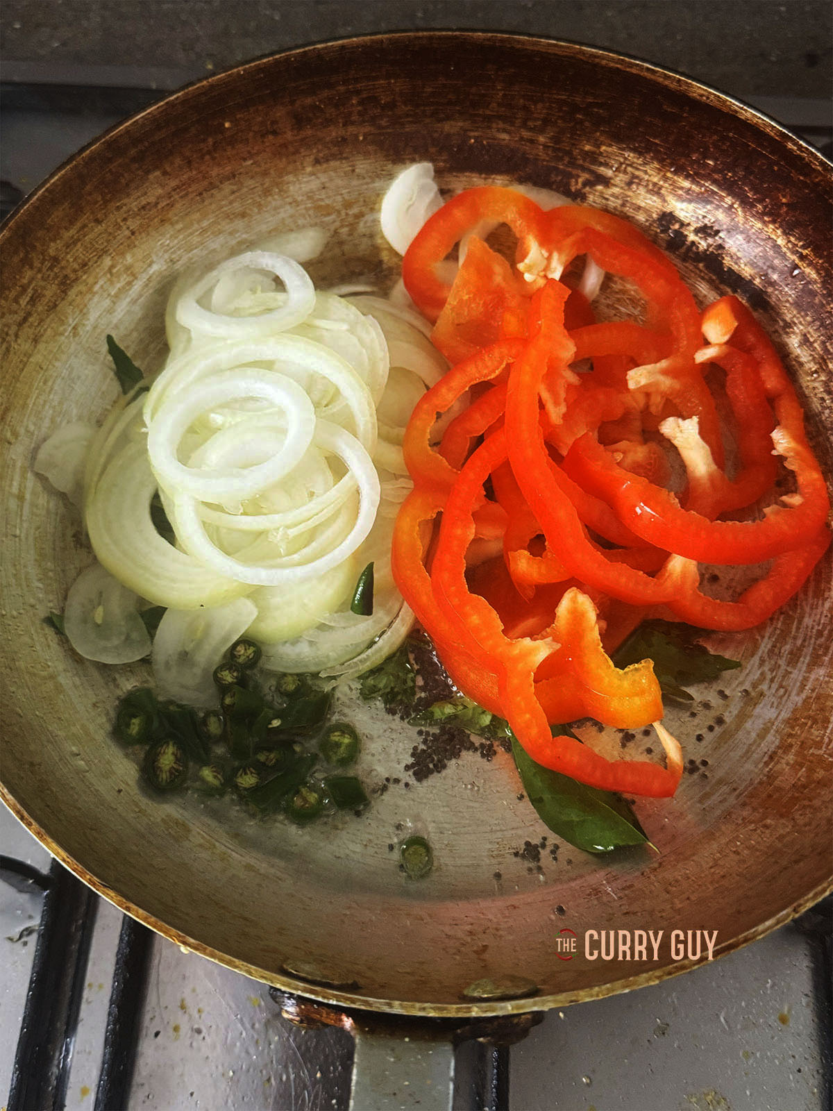 Adding the sliced onion, bell pepper and chillies to the pan.