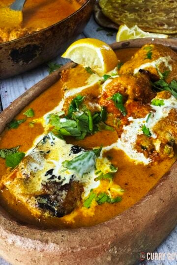 Salmon tikka masala served in a serving bowl garnished with lemon wedge and chopped coriander.