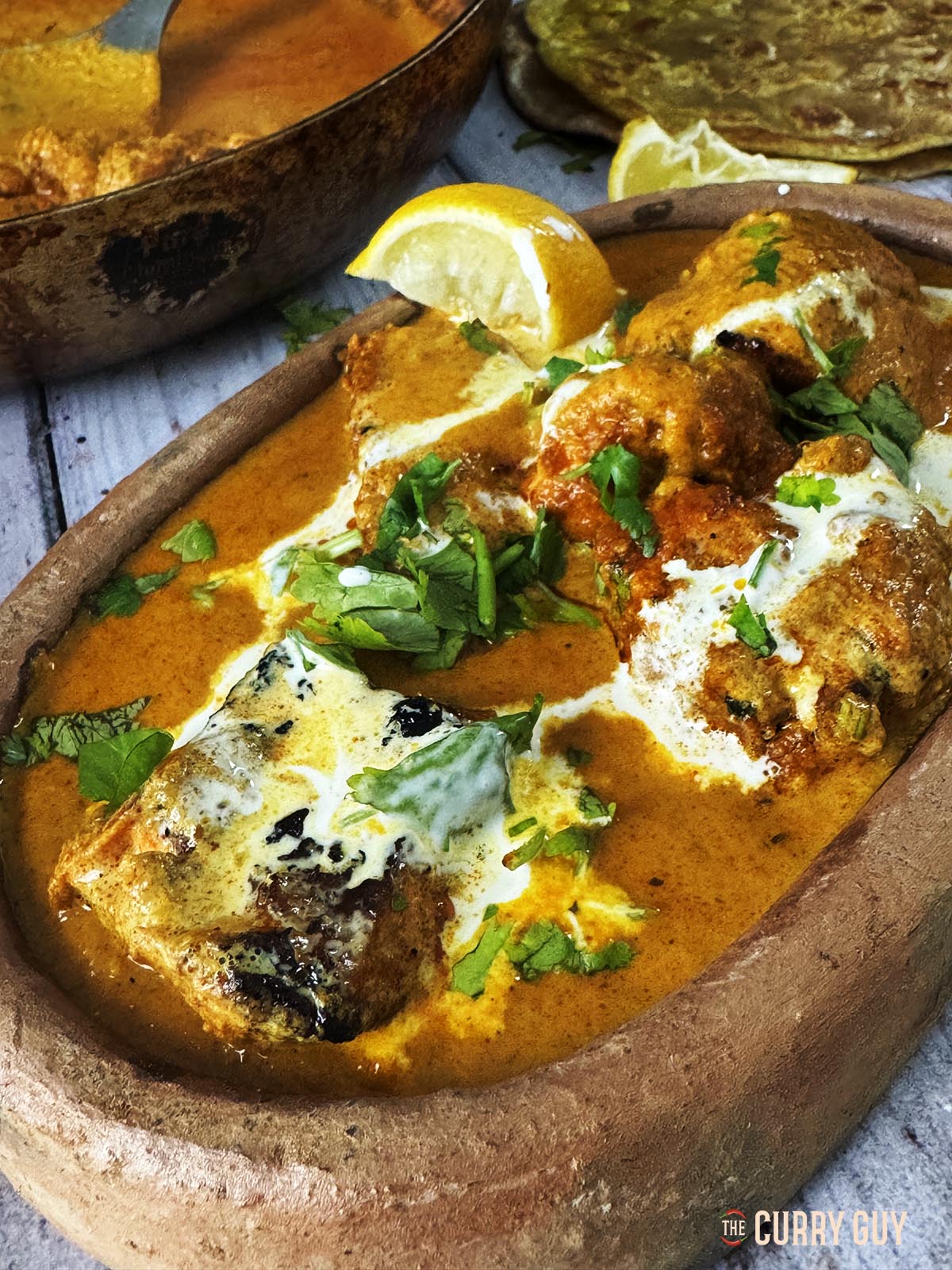 Salmon tikka masala served in a serving bowl garnished with lemon wedge and chopped coriander.
