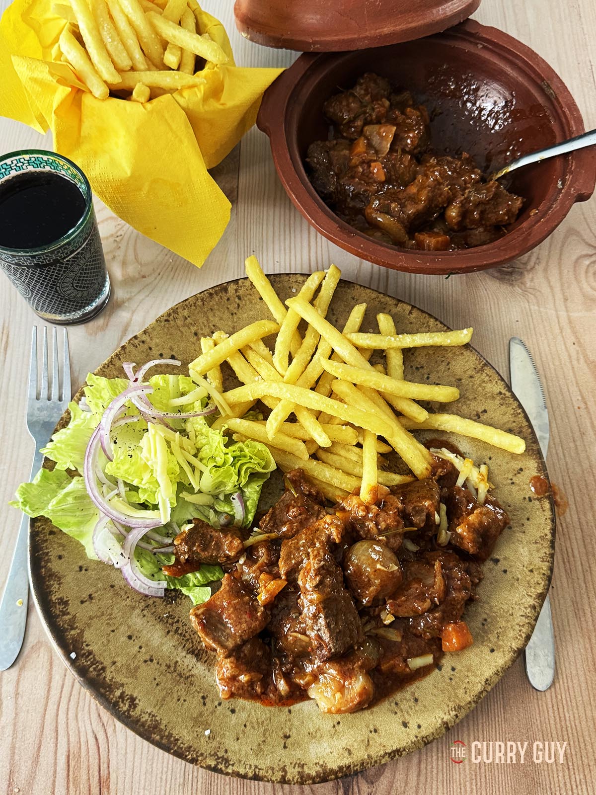 The finished beef stifado on a serving plate with French fries.