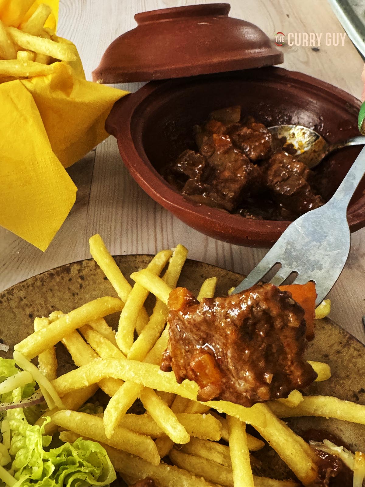 Beef stifado on a serving plate with French fries.