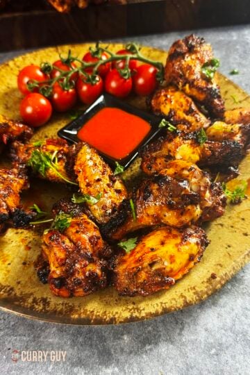 Turkish chicken wings on a serving plate with hot sauce and cherry tomatoes.