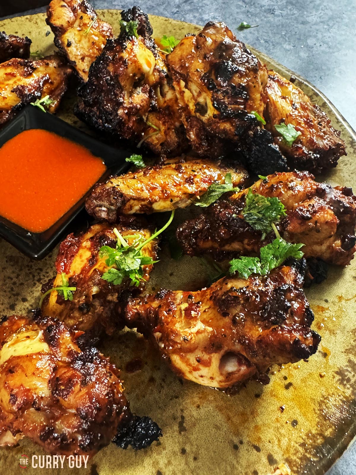 Tandoori Turkish chicken wings with hot sauce served on a plate and garnished with chopped parsley.