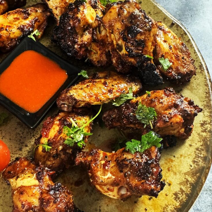 Turkish chicken wings with tomatoes and hot sauce on a serving plate.