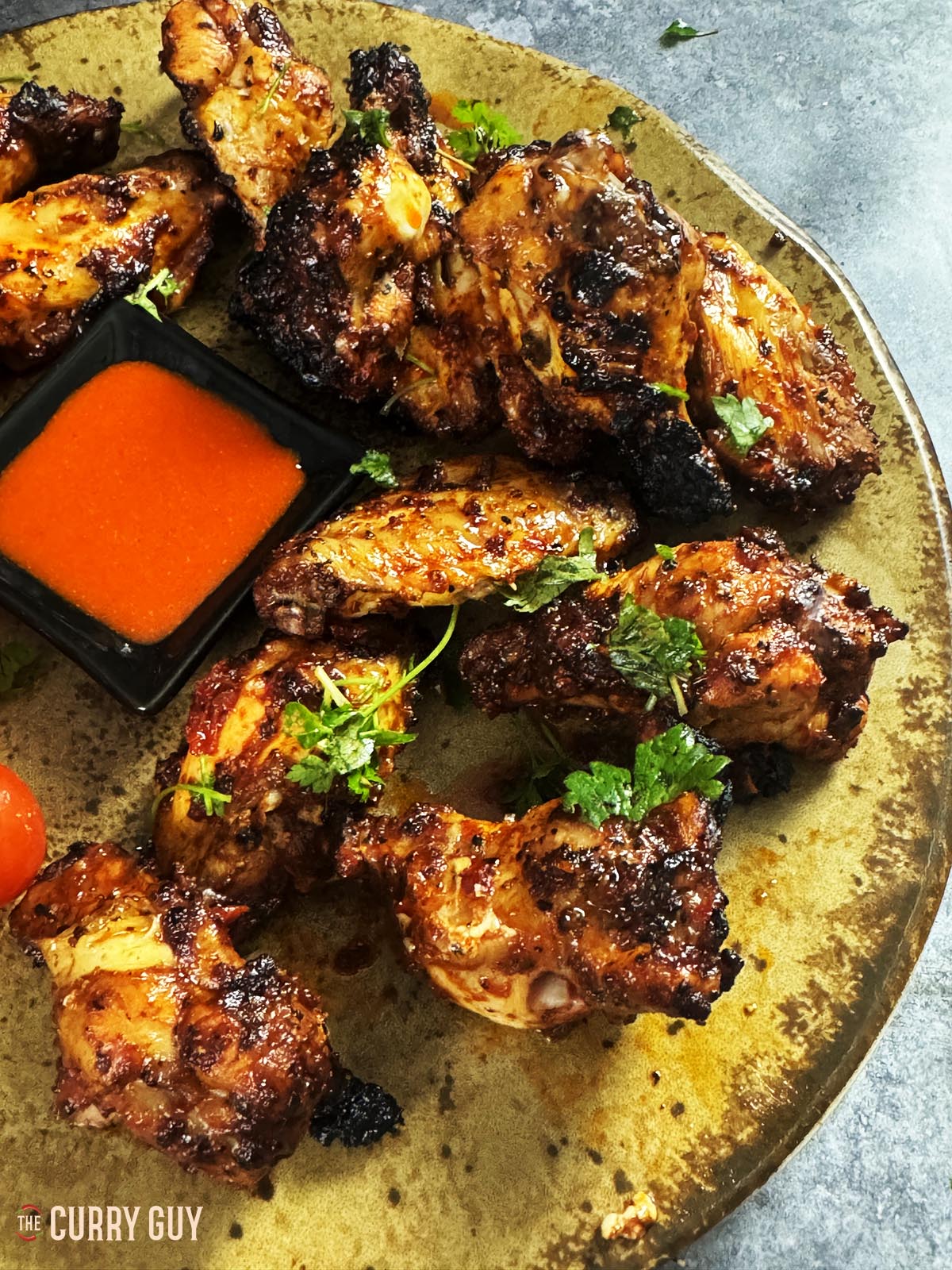 Turkish chicken wings with tomatoes and hot sauce on a serving plate.