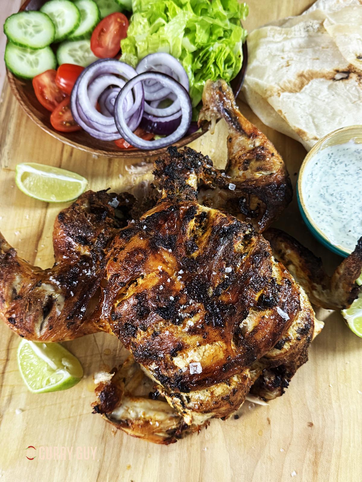 Slow cooker tandoori chicken on a serving platter with raita, bread and salad vegetables. 