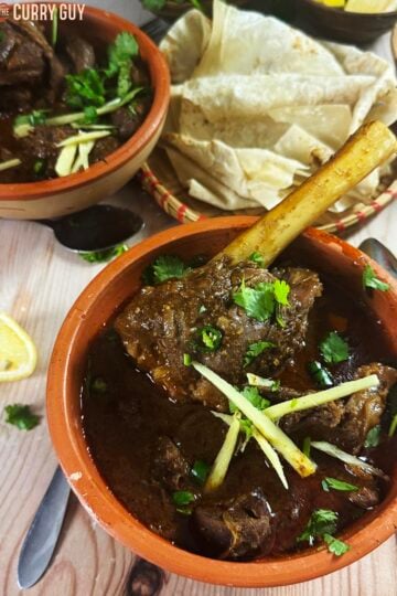Slow cooker nihari in a serving bowl garnished with julienned ginger, chopped green chillies and chopped coriander (cilantro).