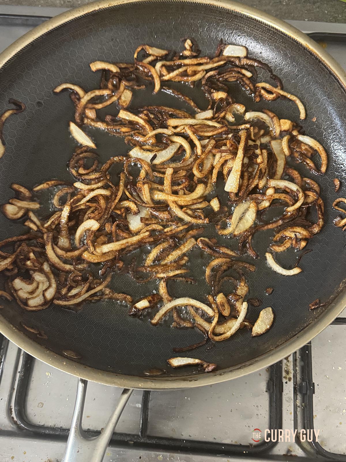 Frying the onions in the oil until dark golden brown.