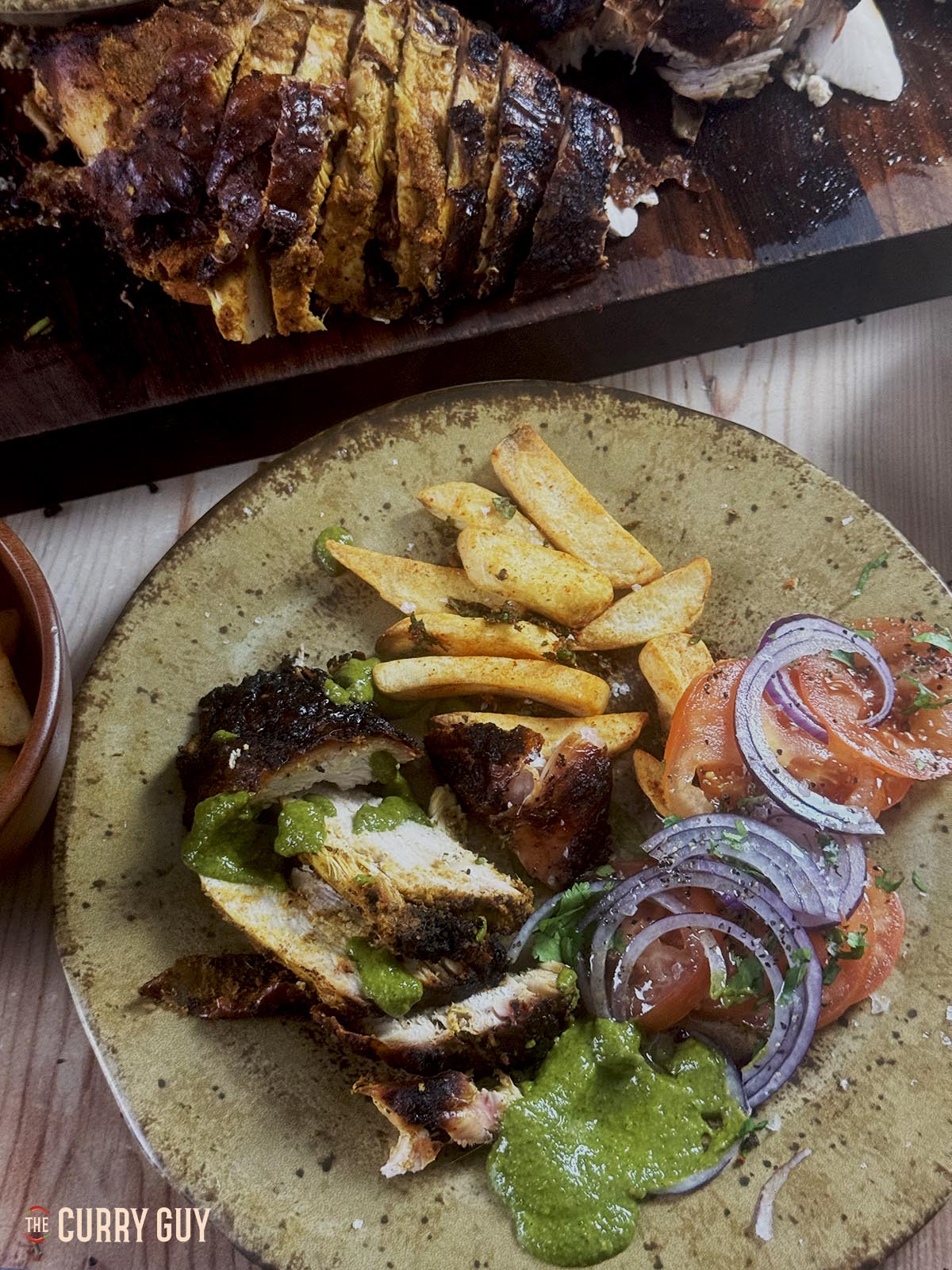 Tandoori turkey crown on a serving plate with chips, onion salad and coriander chutney.