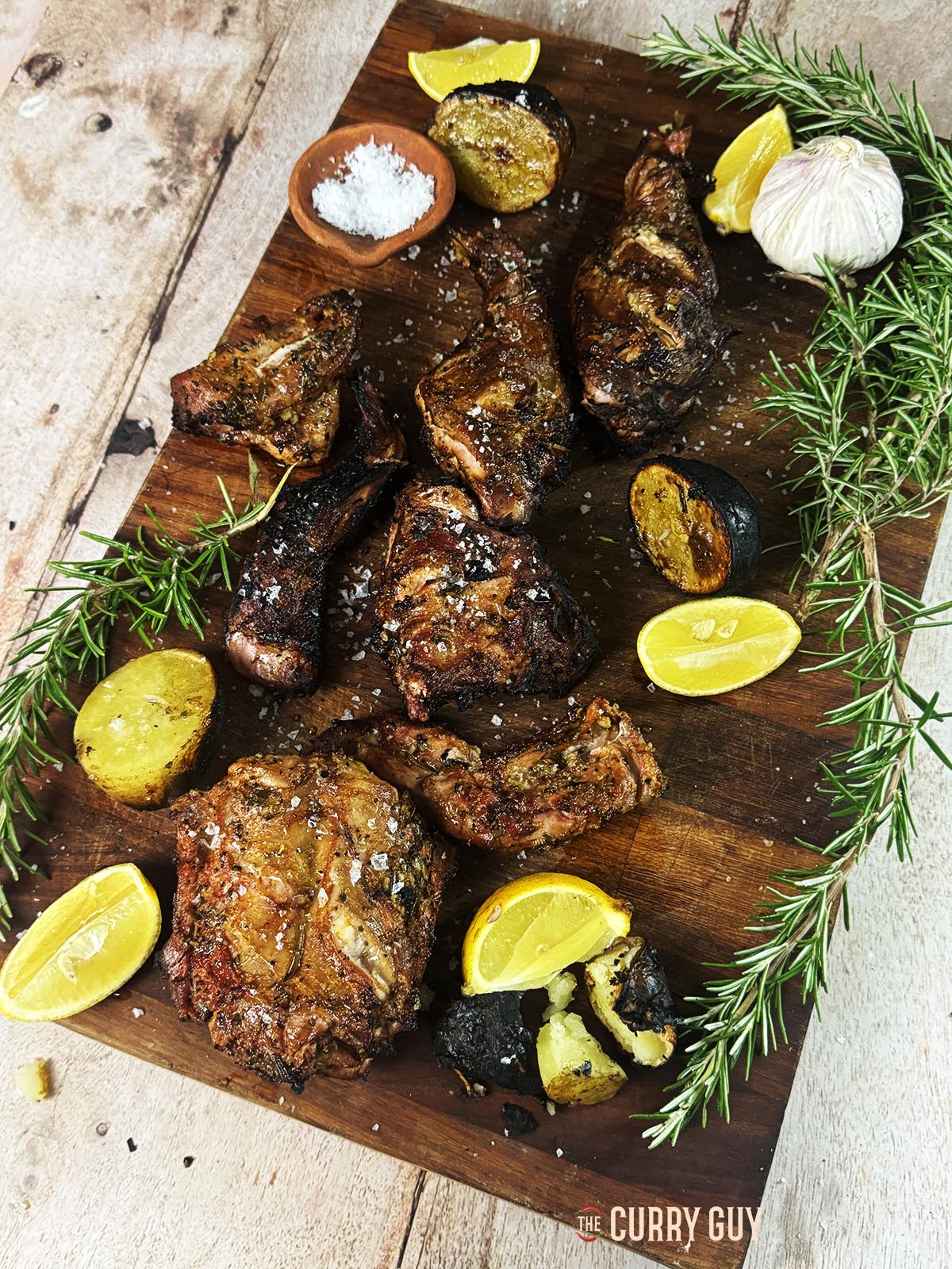 Grilled rabbit on a serving board with lemon wedges to squeeze over the top.