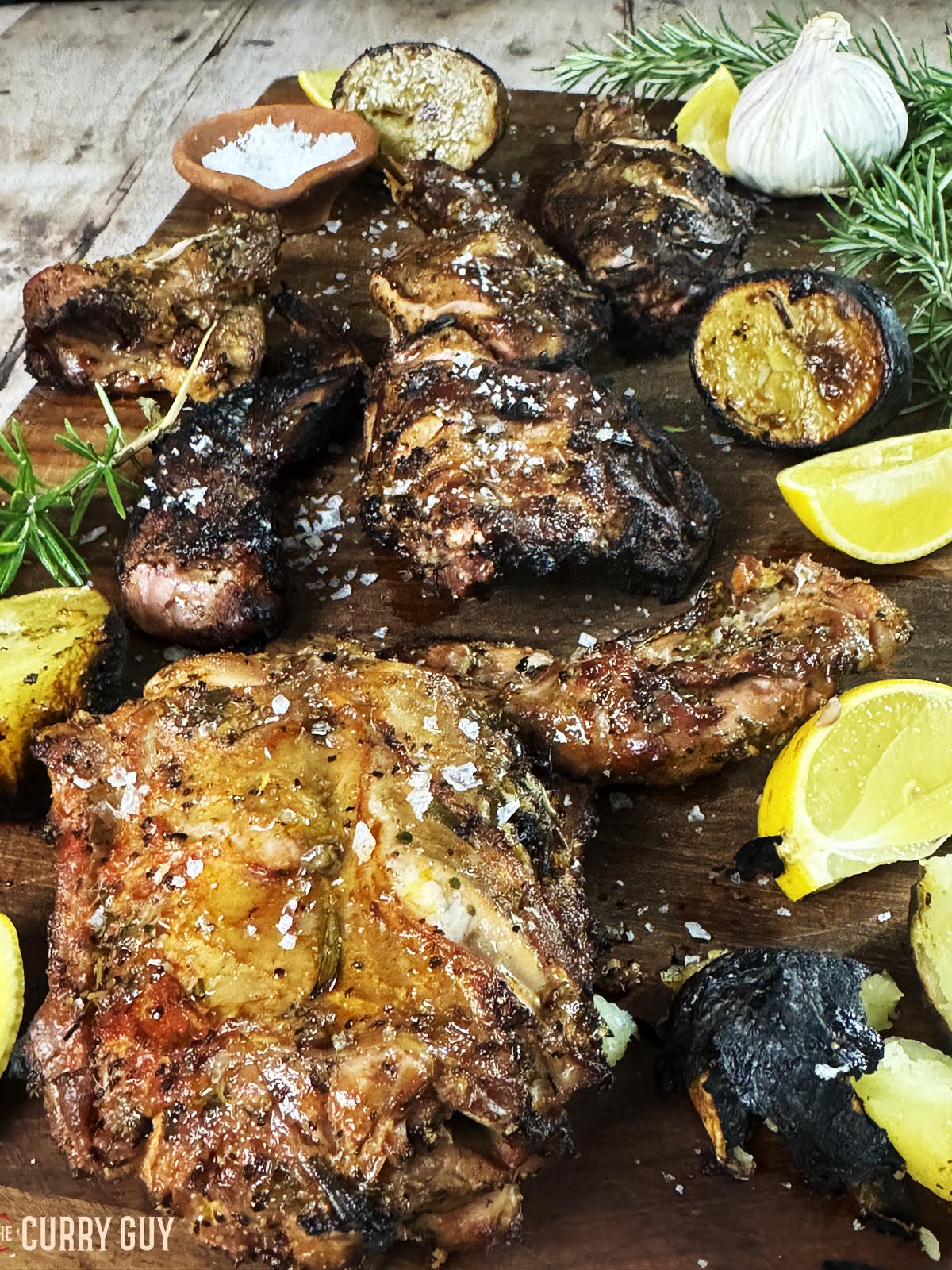 Grilled rabbit on a serving board with the cooked potatoes and lemon wedges.