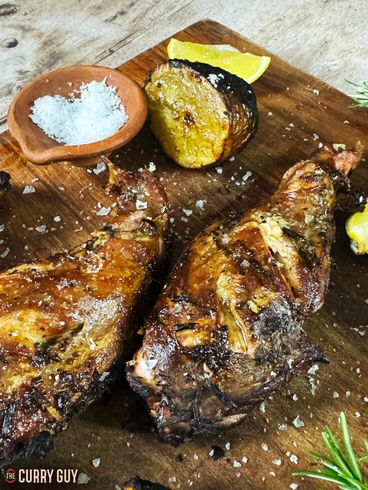 Grilled rabbit on a serving board with lemon wedges.
