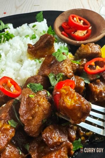 Babi kecap served with rice on a serving plate, garnished with sliced spur chillies.