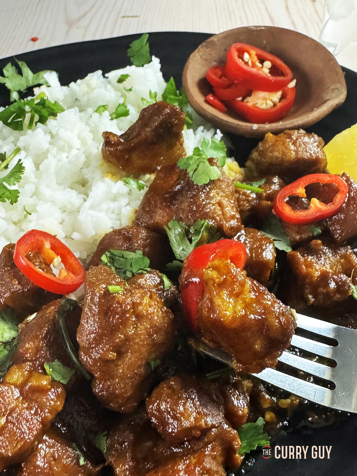 Babi kecap served with rice on a serving plate, garnished with sliced spur chillies.