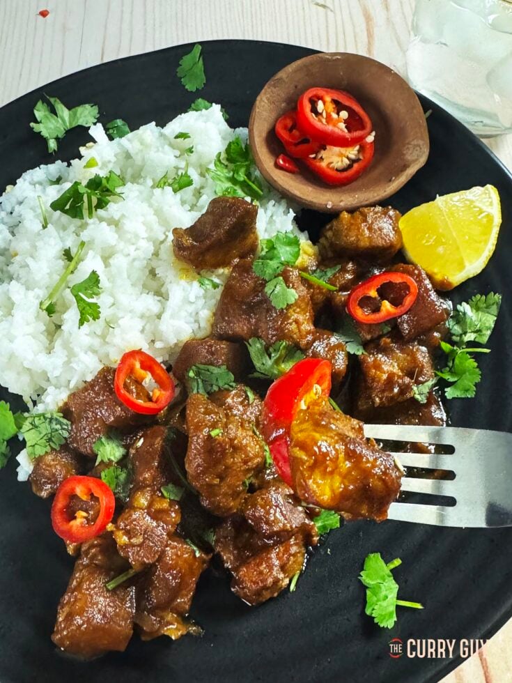 Slow cooker babi kecap on a serving plate, garnished with sliced chillies over rice.