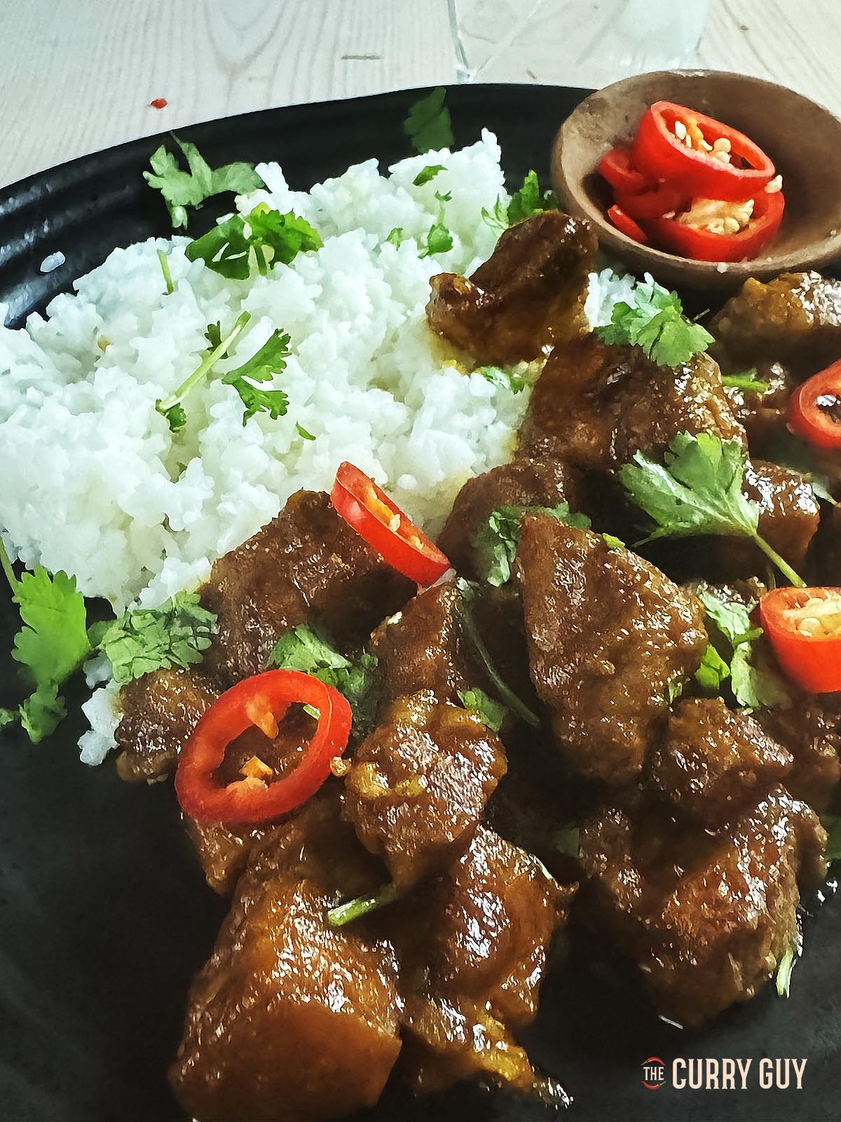 Babi kecap on a serving plate with rice and garnished with sliced chillies and fresh coriander.