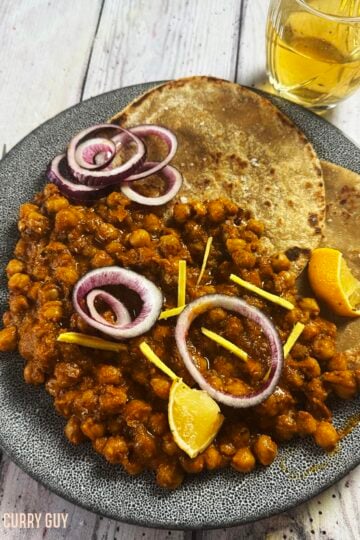 Slow cooker chana masala curry on a plate, garnished with red onion rings and lemon wedges.
