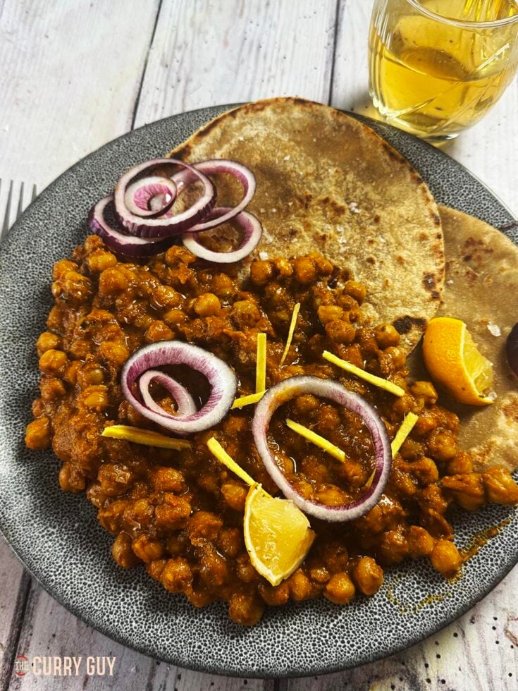 Slow cooker chana masala curry on a plate, garnished with red onion rings and lemon wedges.
