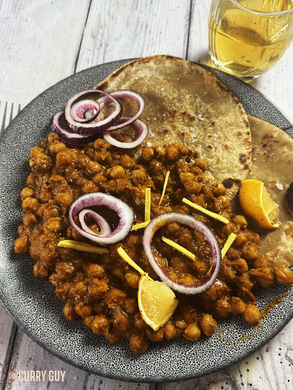 Slow cooker chana masala curry on a plate, garnished with red onion rings and lemon wedges.