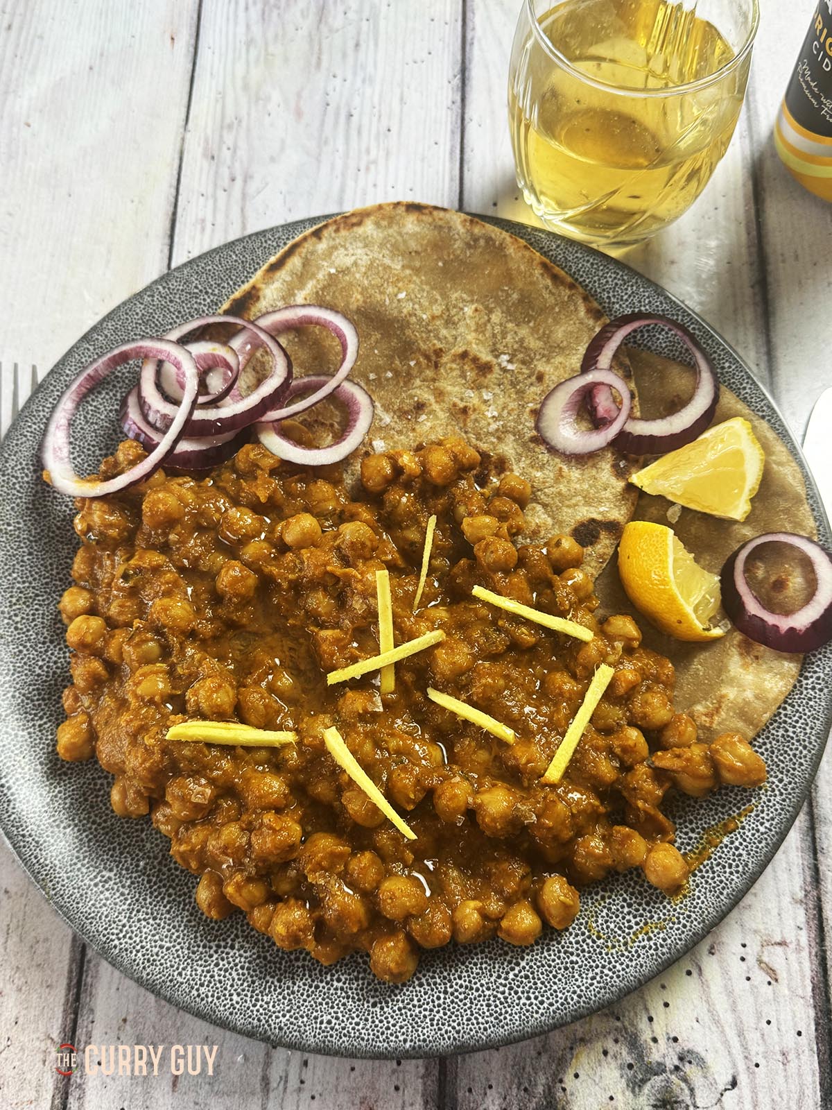 Slow cooker chickpea curry on a serving plate with parathas and garnished with lemon wedges, julienned ginger and red onion rings.