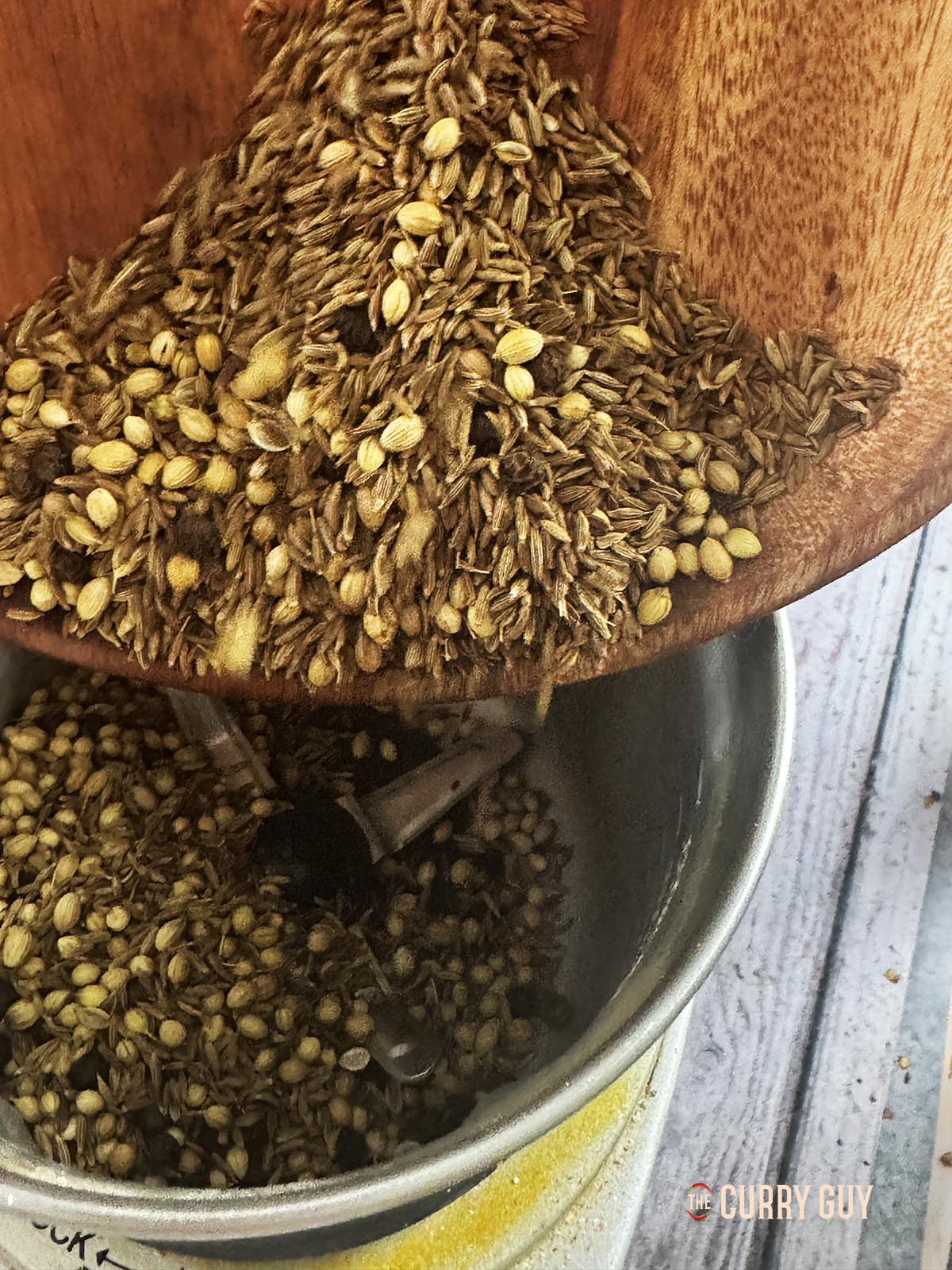 Adding the roasted spices to a spice grinder. 