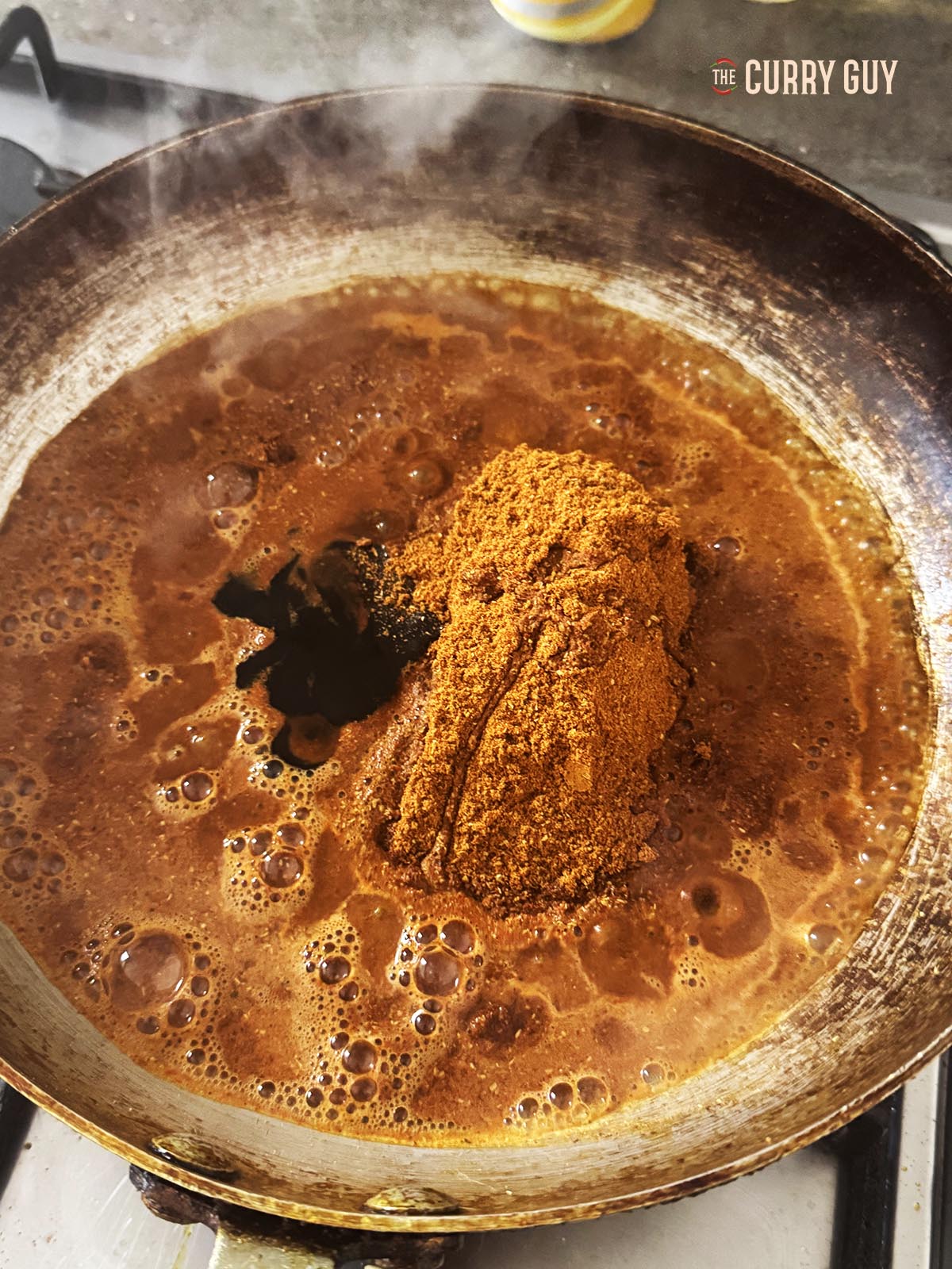 Adding the ground spice blend to a pan over a medium heat with the water and tamarind concentrate.