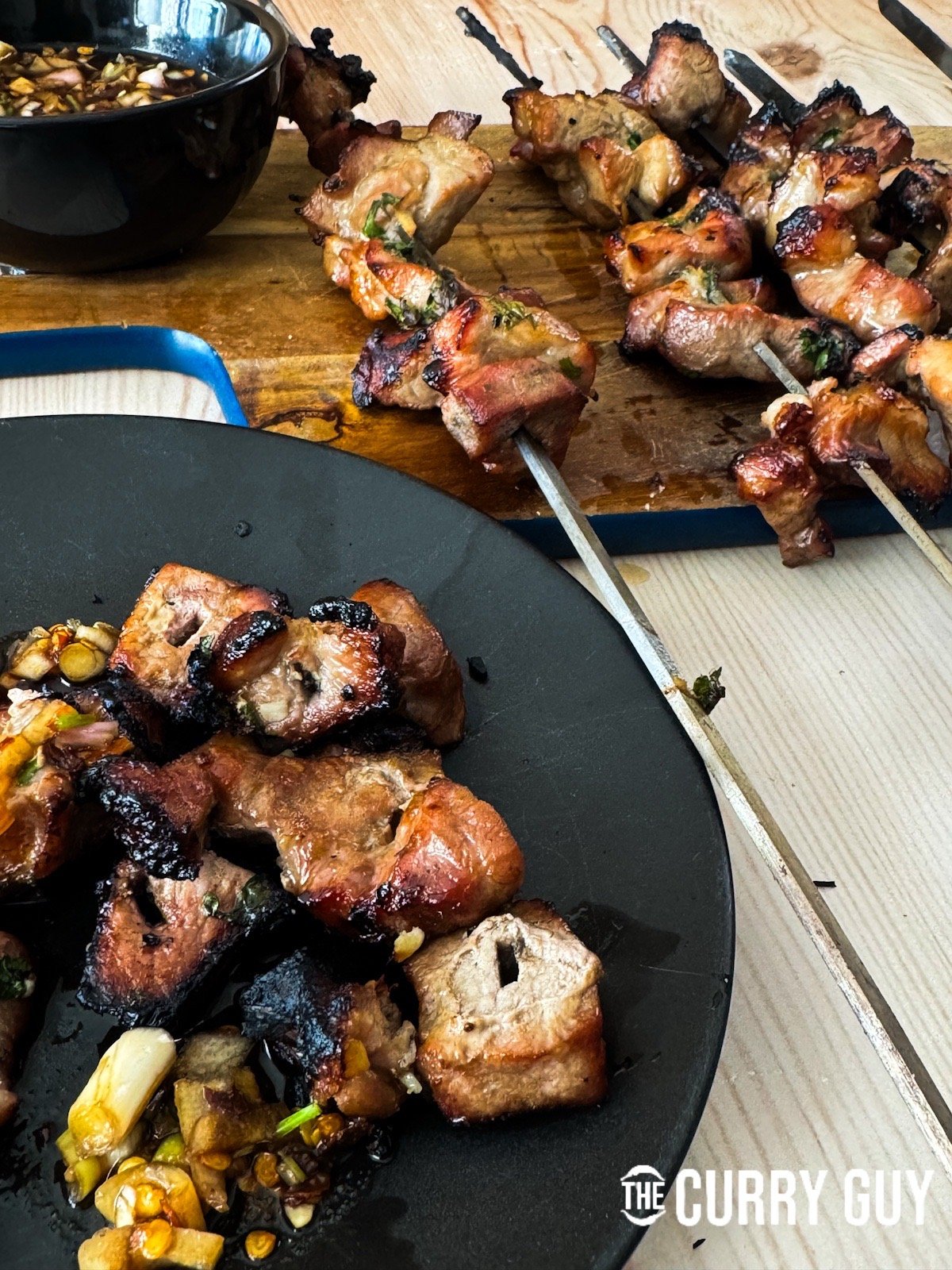 Thai pork skewers with a plate stacked with pork and nam jim jaew sauce.