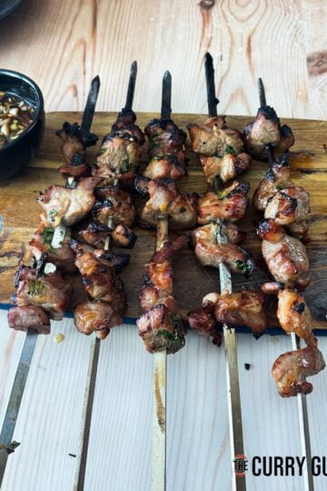 The pork skewers resting on a serving board next to nam Jim jaew sauce.