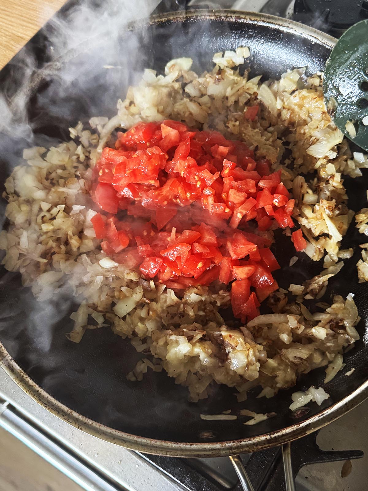 Adding chopped tomatoes to the fried onion mixture.