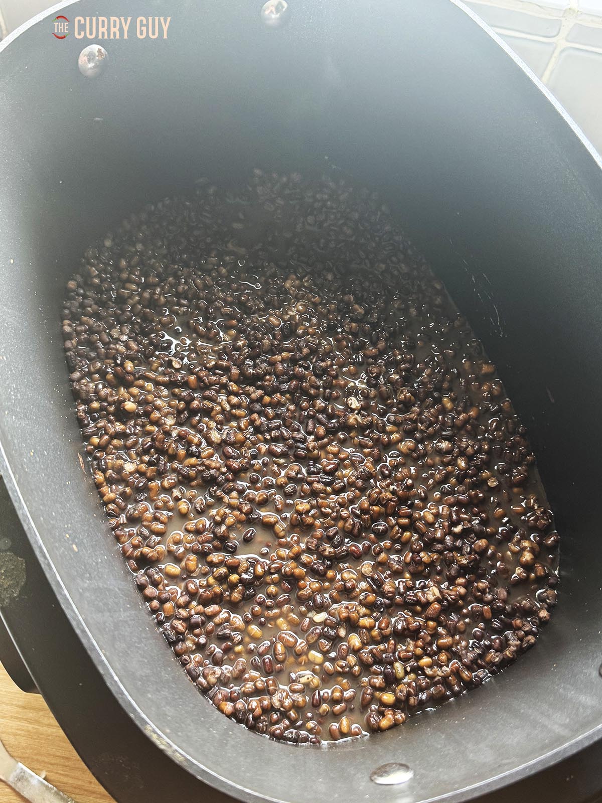 Black urad dal in a slow cooker covered with water.