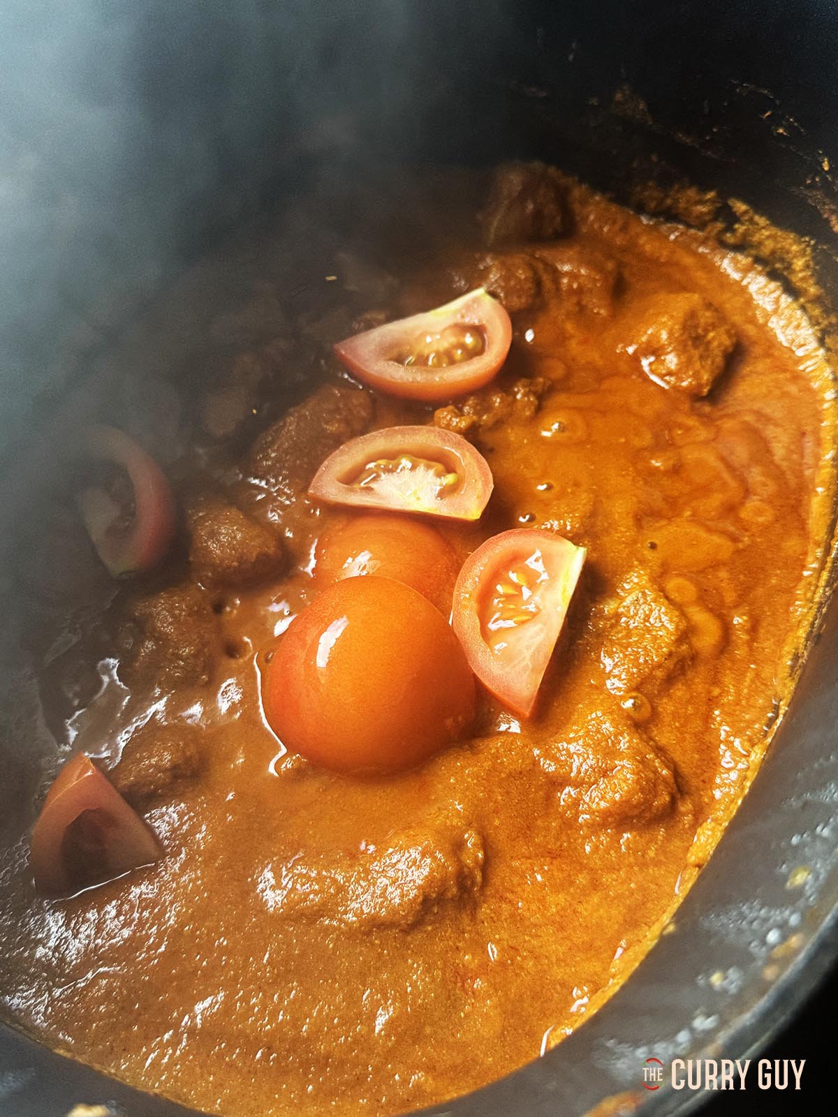 Adding the quartered tomatoes to the curry.