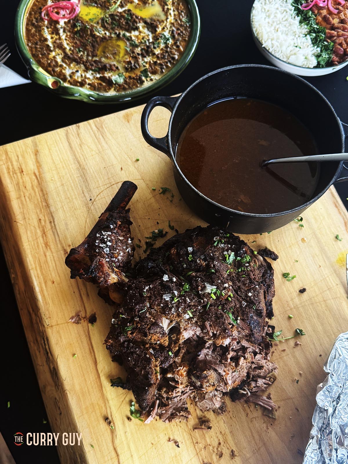 Slow cooker lamb raan on a serving platter next to a pot with the meat juices.