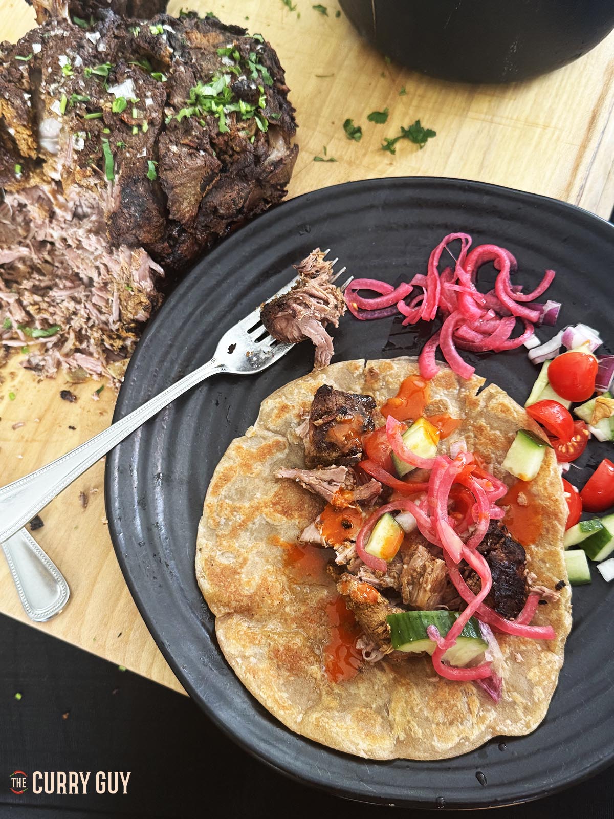 Lamb raan on a flatbread topped with garnishes to wrap up.