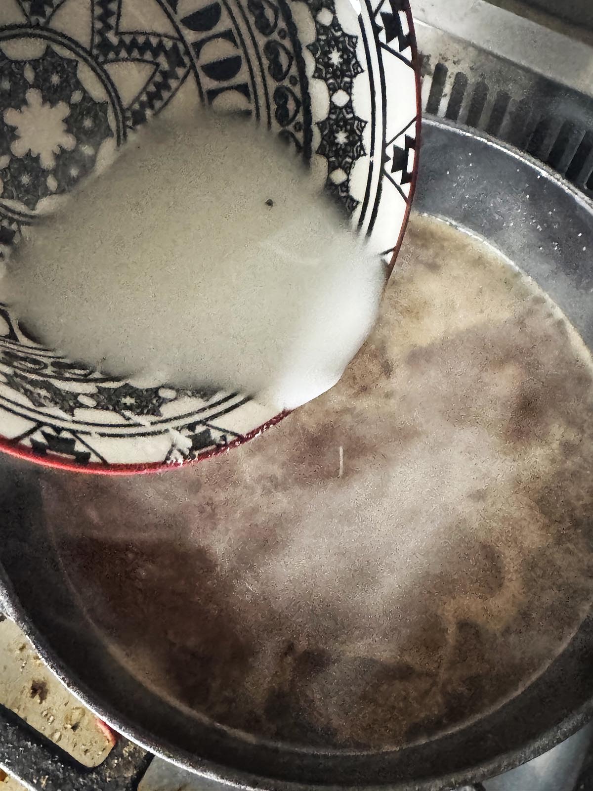 Adding the slurry to thicken the sauce.