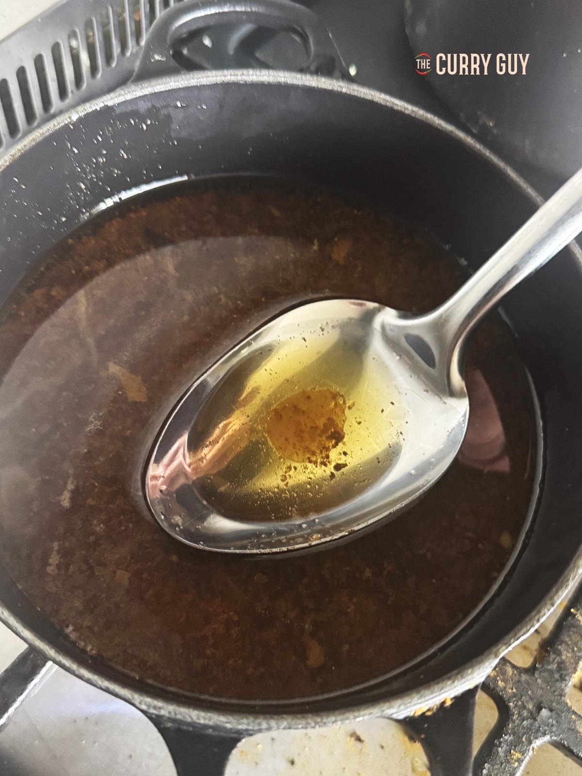 Skimming the oil off the top of the meat juices in a pan.