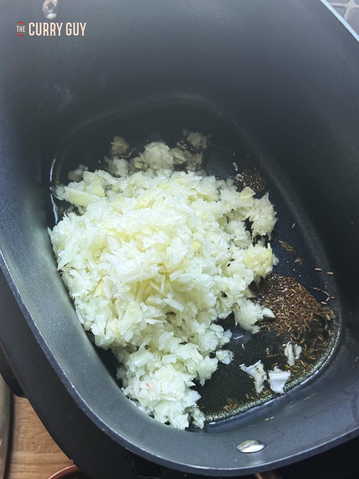 Adding the chopped onions and a pinch of salt to the hot oil and cumin seeds.