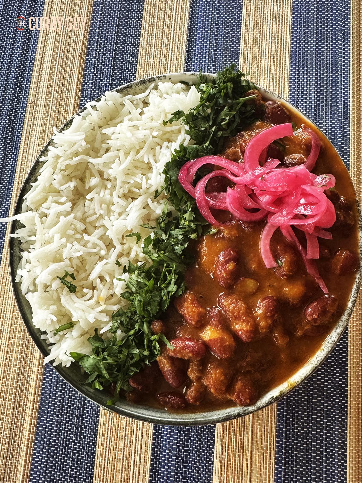 Slow cooker rajma curry in a serving bowl, garnished with coriander (cilantro) and pickled onion.