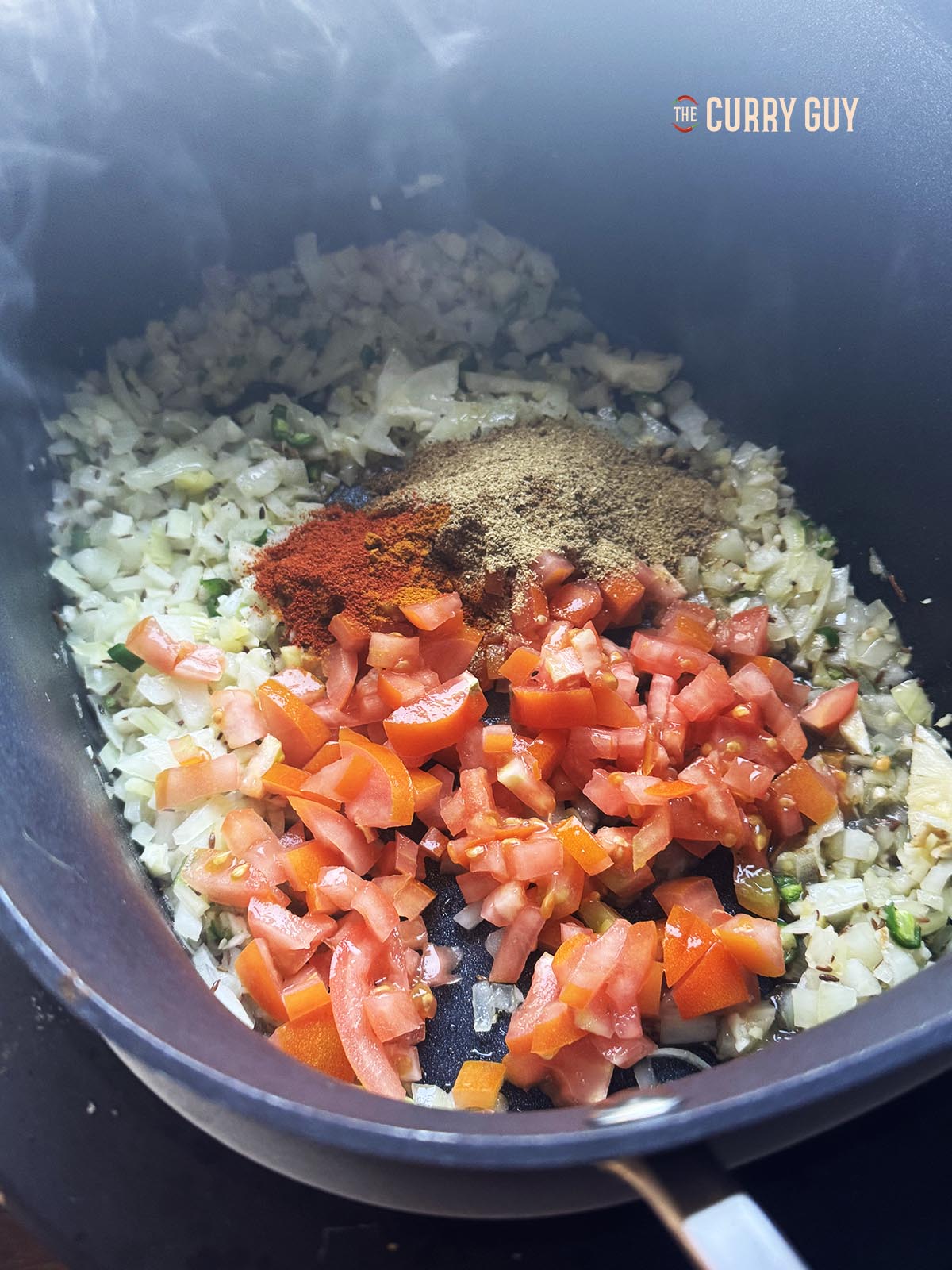 Adding the chopped tomatoes and ground spices to the onion mixture in the slow cooker.